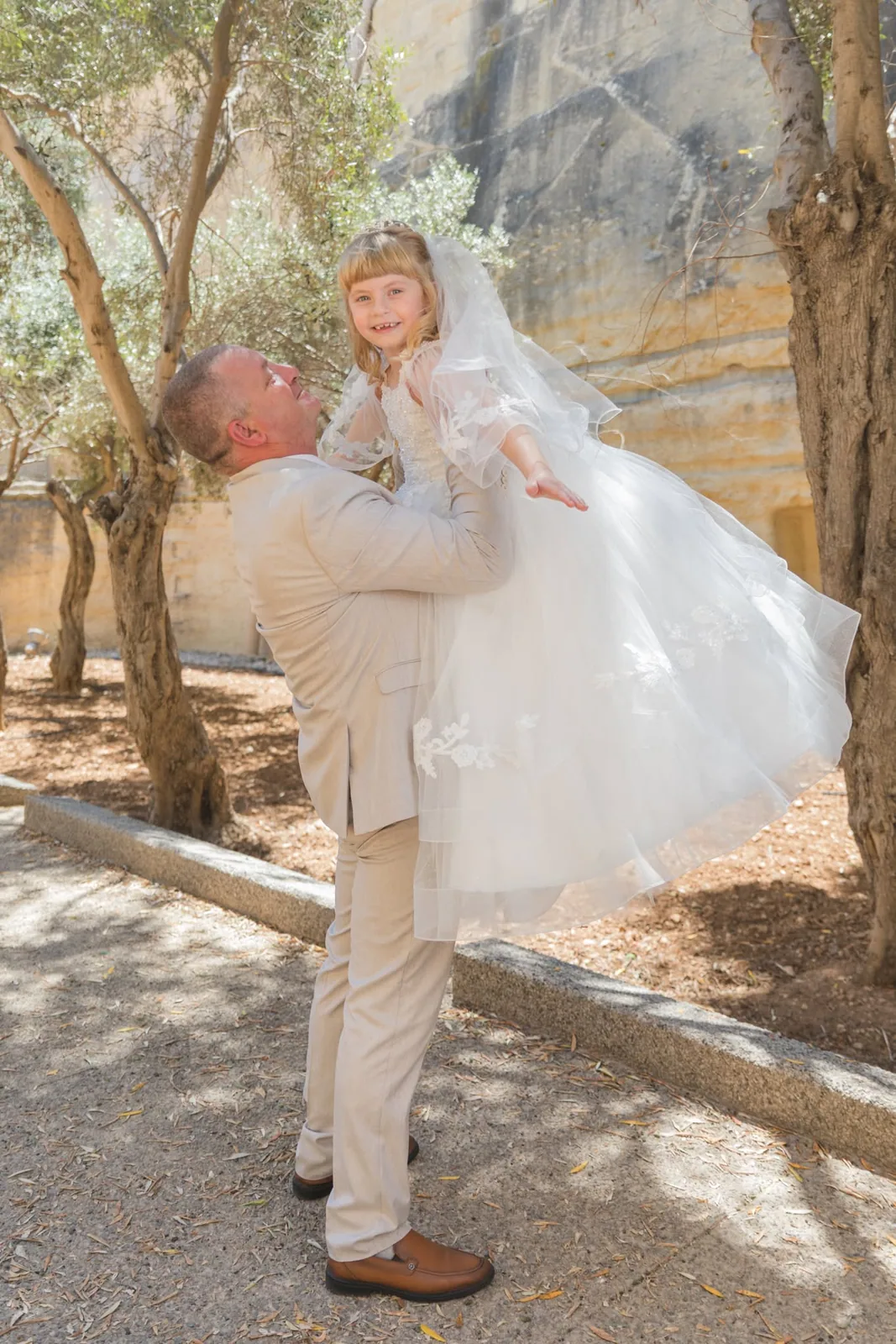 father lifting daughter in communion dress malta