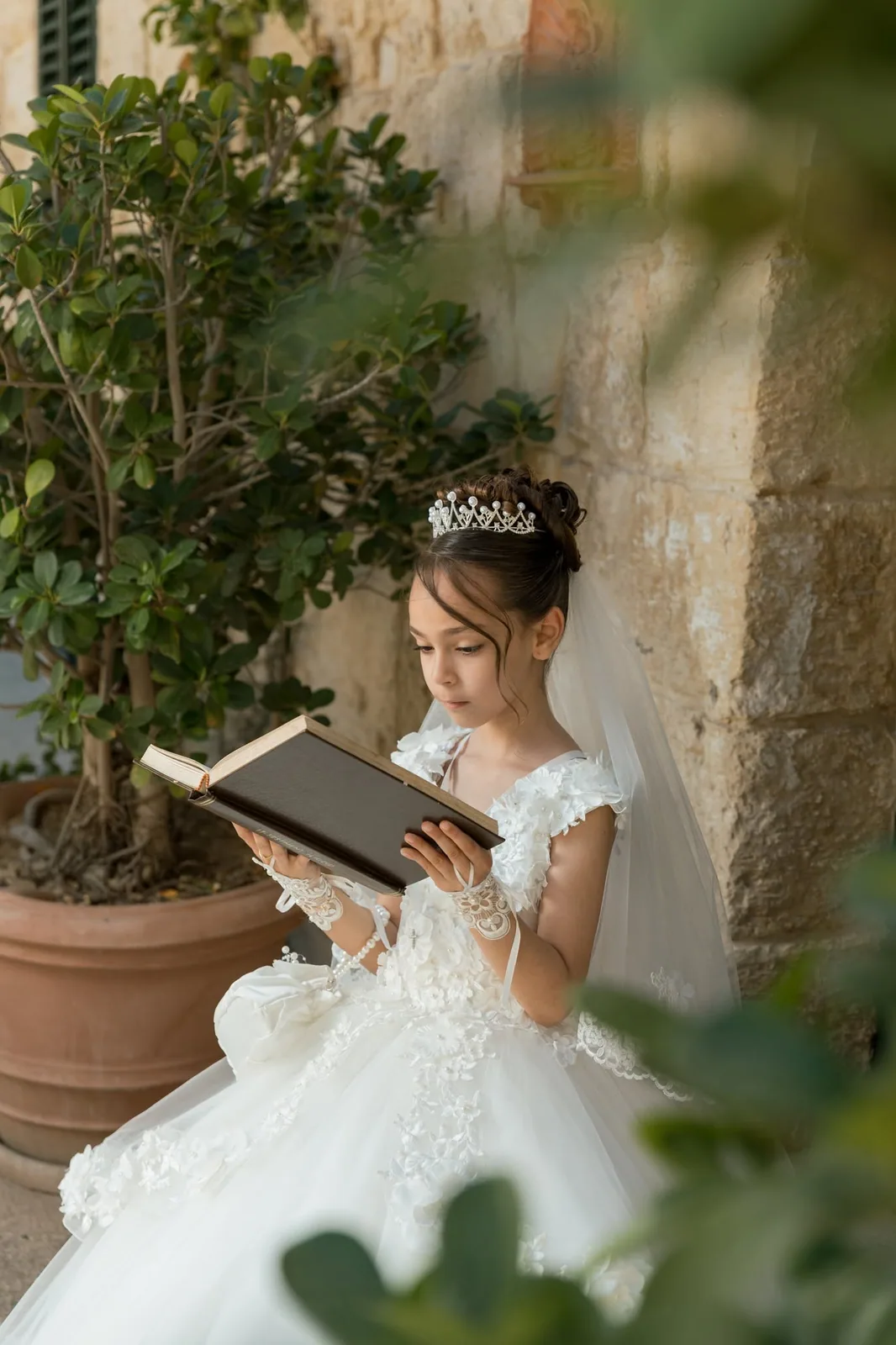 A girl in her First Communion dress reading beside a limestone wall in Malta