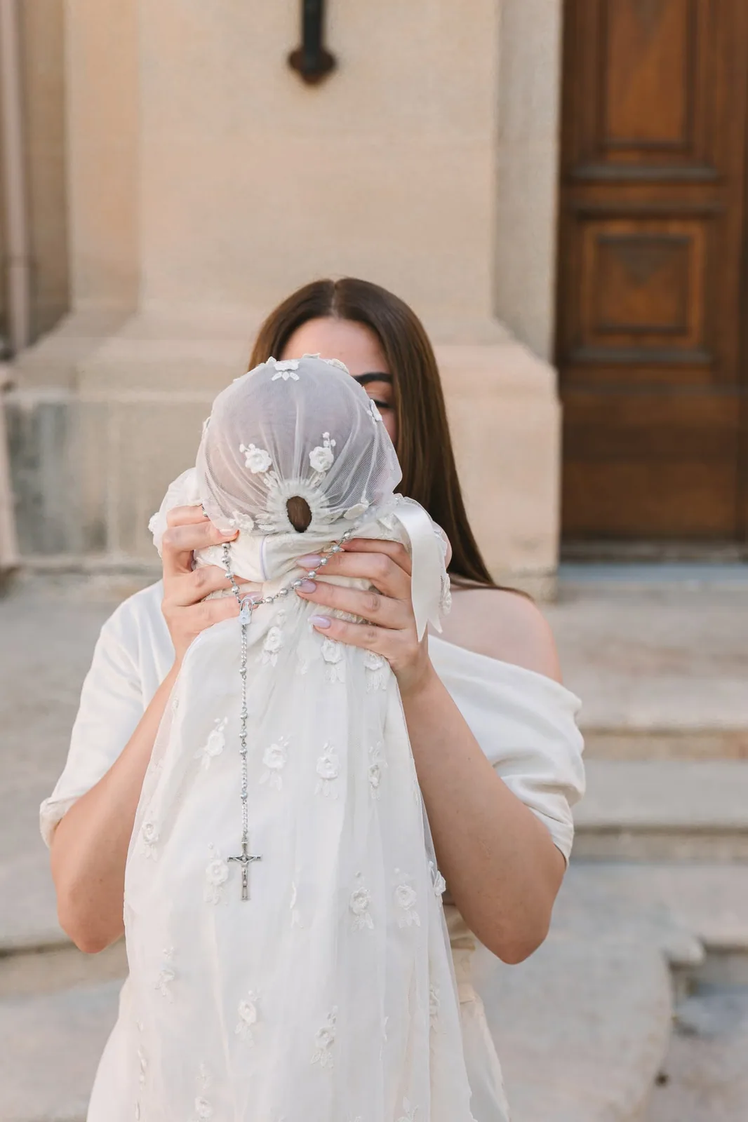 A girl holding a white christening gown in front of her outside a doorway.