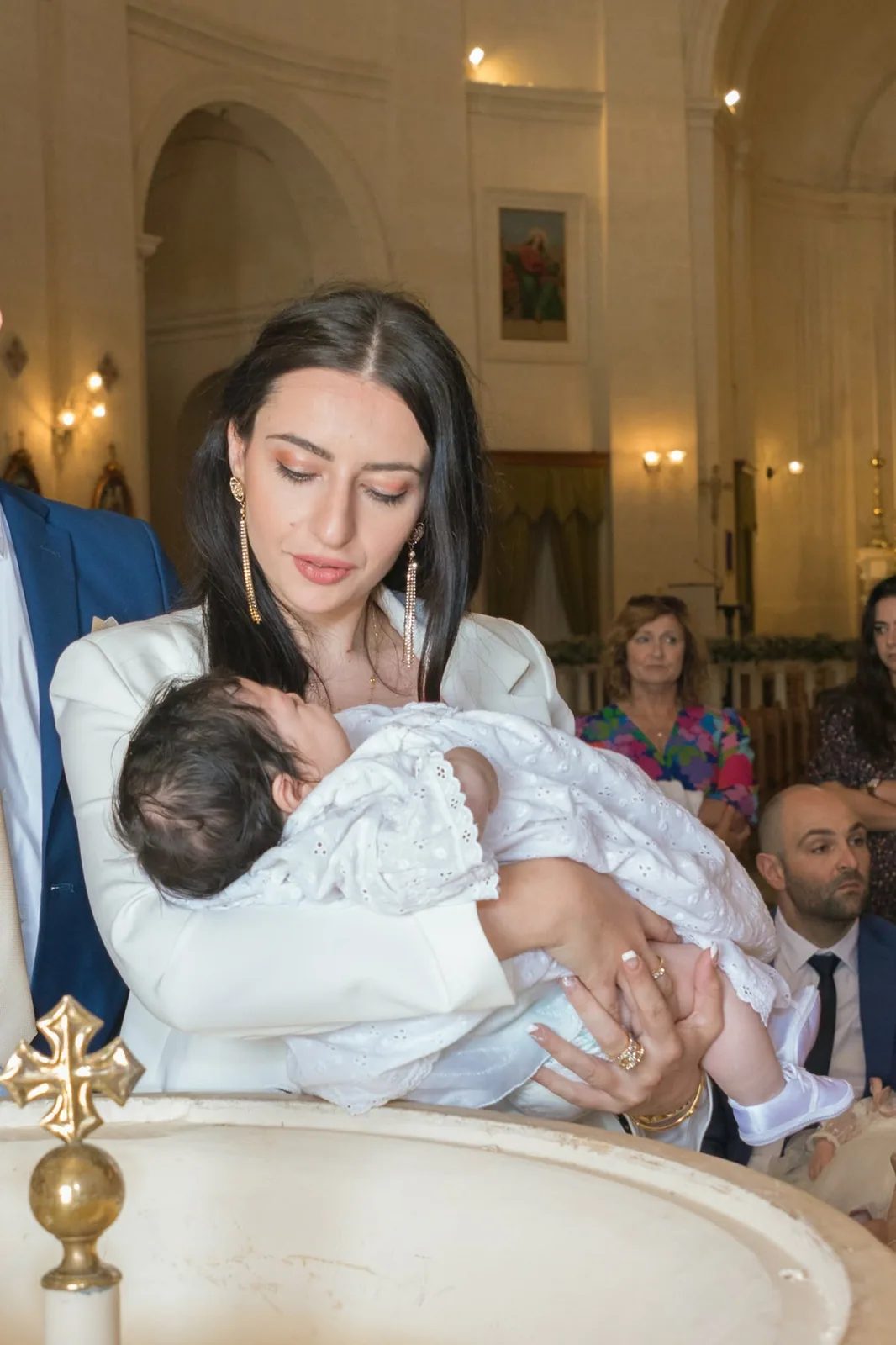 mother holding baby beside baptism font malta