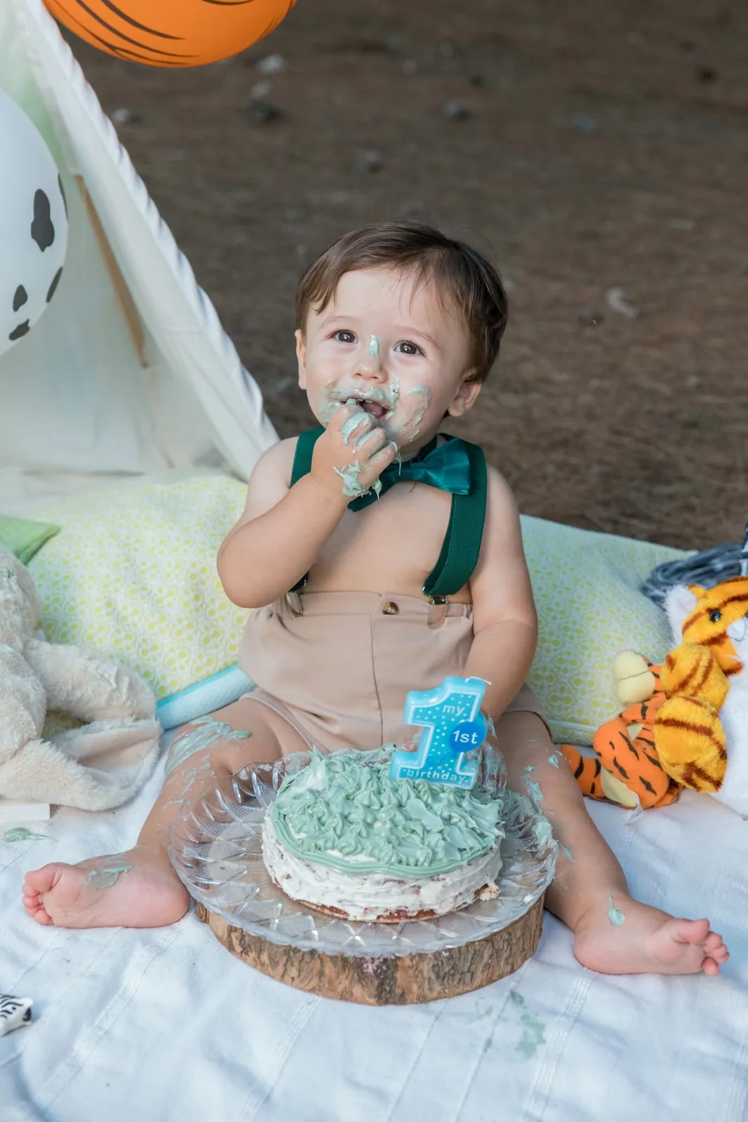 A toddler tasting blue birthday cake beside a teepee and sports-themed decorations in Malta