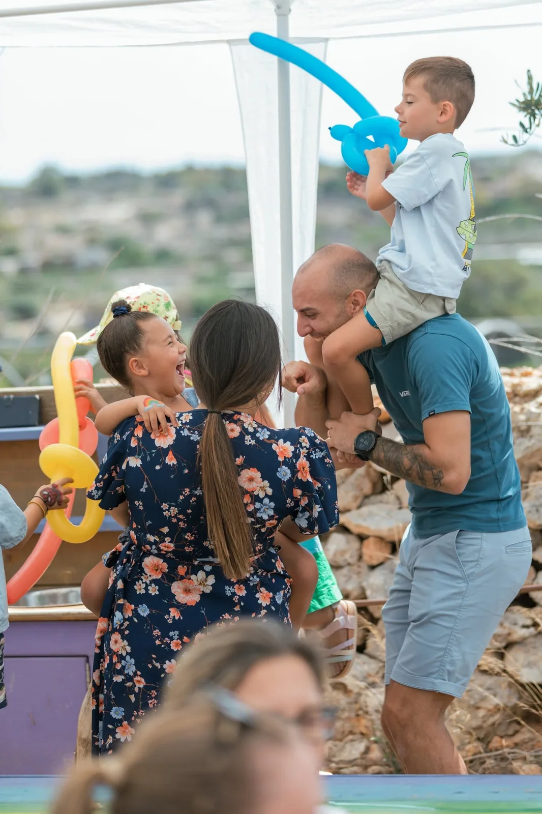 A man carrying a child on his shoulders at an outdoor party.