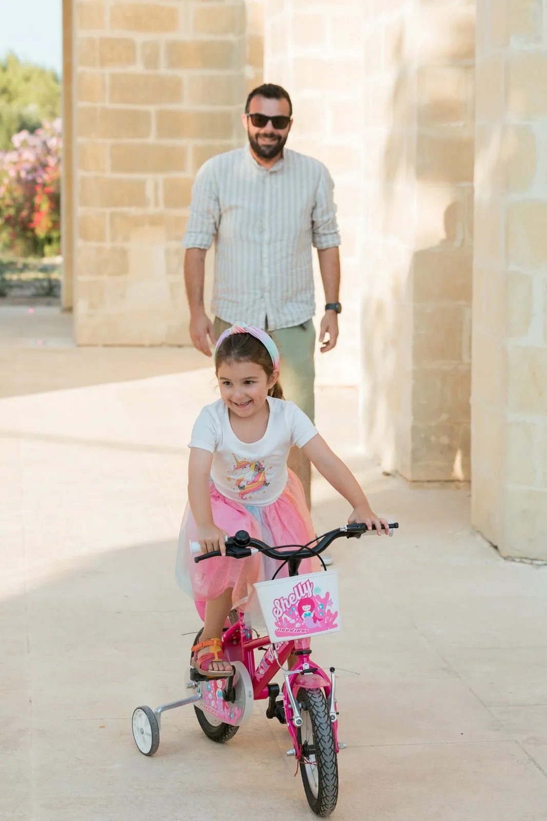 father watching daughter ride pink bicycle malta