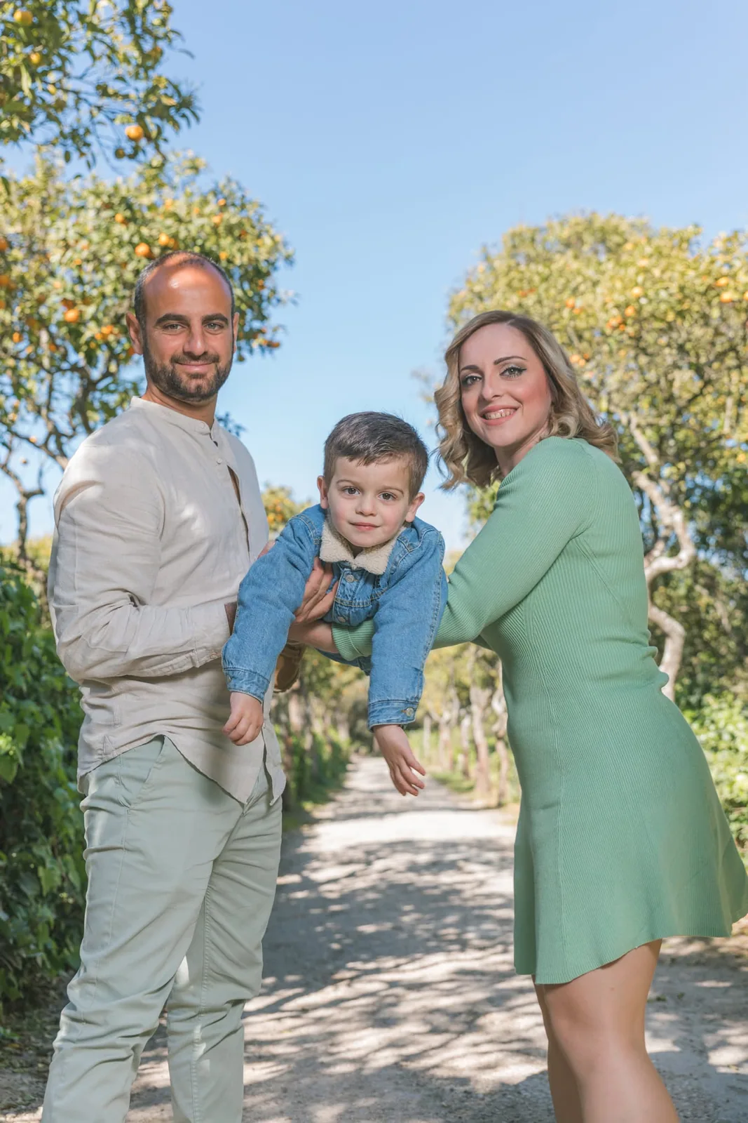Parents playfully lifting their toddler together in a sunlit garden in Malta