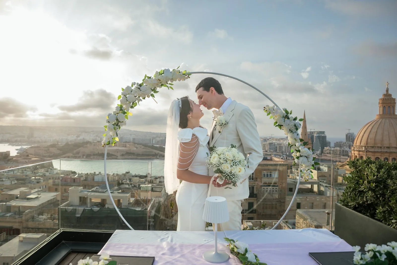 bride and groom kissing under floral arch malta