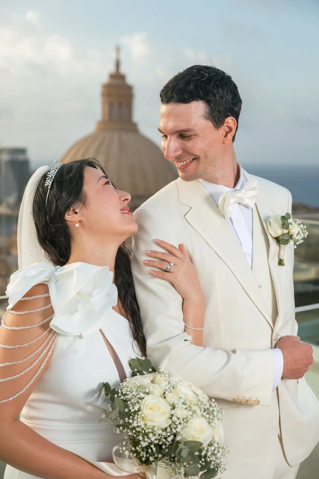 A bride and groom smiling at each other on a rooftop overlooking Malta