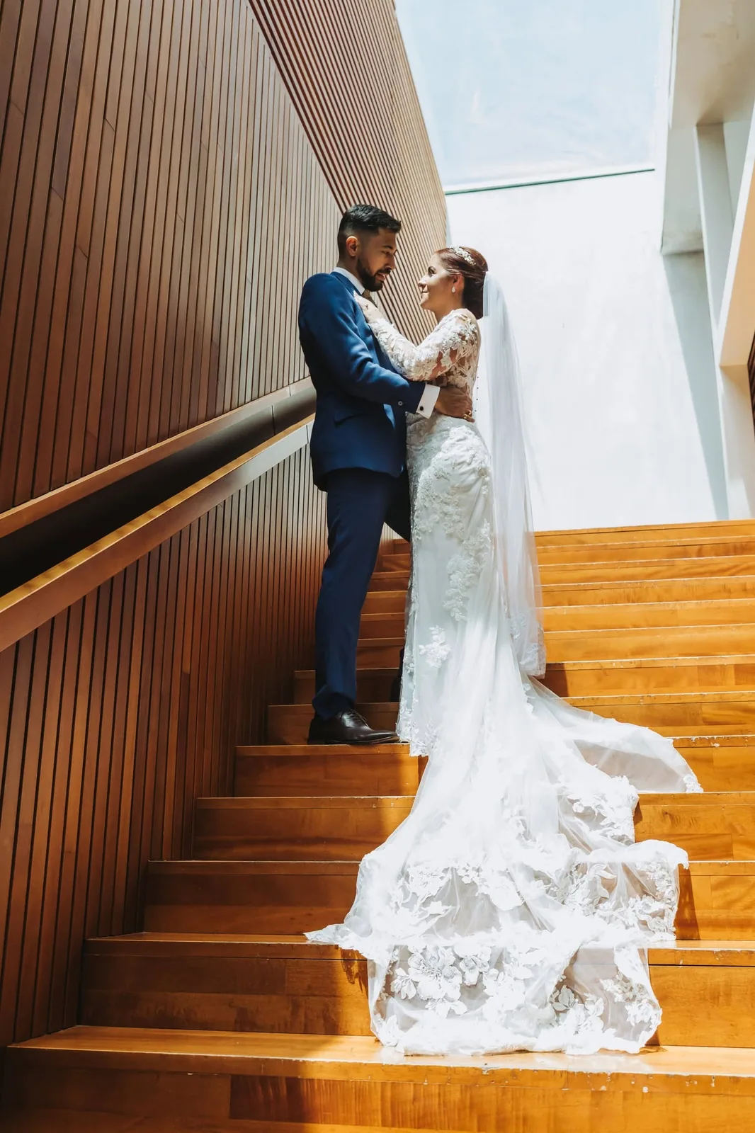 A bride and groom embracing on a wooden staircase, with her lace train flowing down the steps in Malta