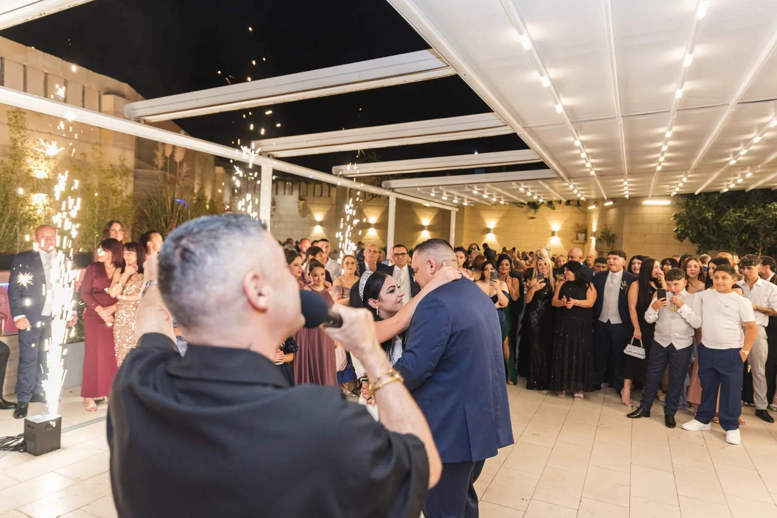 A bride and groom dancing beside a singer and sparklers, surrounded by wedding guests in Malta